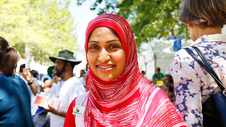 A smiling woman wearing a bright red and silver head scarf.
