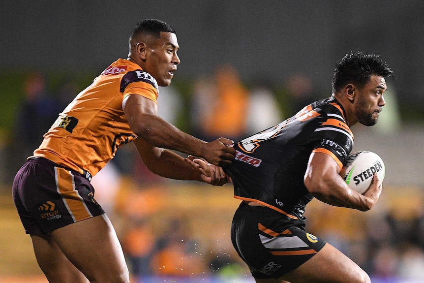 A Brisbane Broncos NRL players holds the jersey of a Wests Tigers opponent as he tries to tackle him.