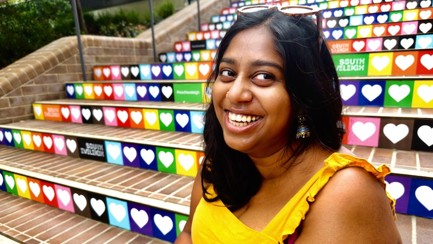 Profile image of Poora Raj sitting on rainbow-coloured steps, smiling to camera.