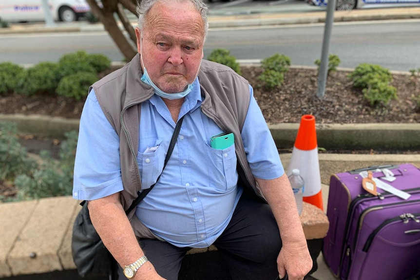 A elderly man sitting on a stone bench on the side of the road at the Queensland border