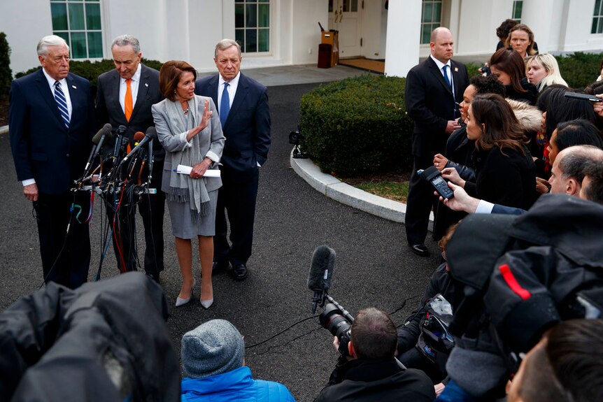 Nancy Pelosi raises her hand, while Steny Hoyer, Chuck Schumer and Dick Durbin stand behind her. They are faced by the media.