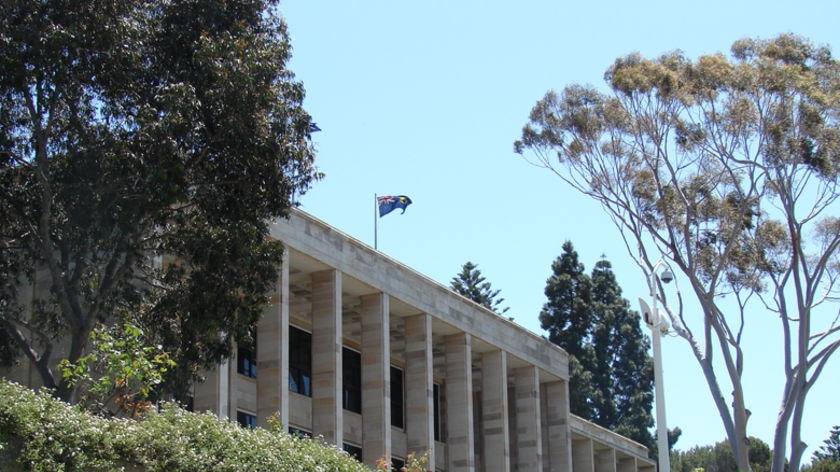 A wide shot of Parliament House in Perth surrounded by trees and blue sky.