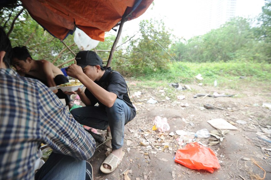 Boys eat noddles in a rubble-strewn field