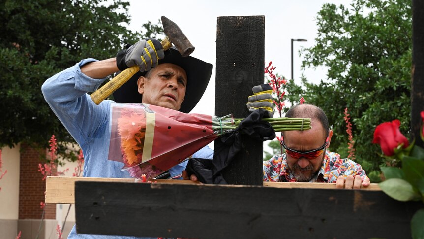 Man nails flowers to a cross with a hammer.