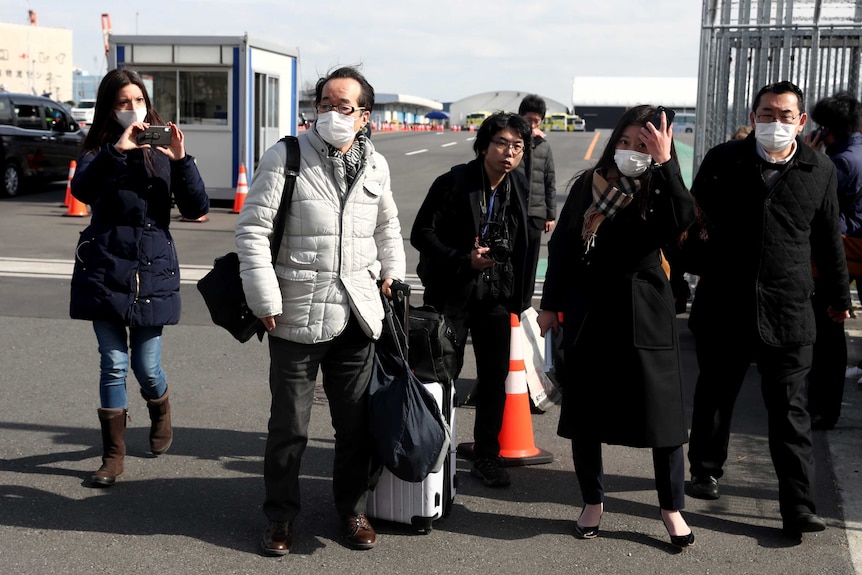 Passengers in face masks walking across a dock