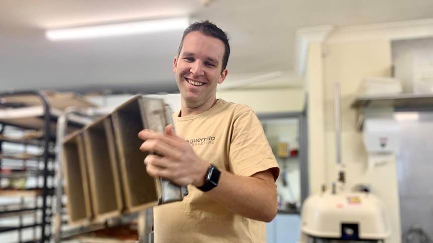 Lagom Bakery co-owner Jon Reeves smiles as he picks up silver bread tins.