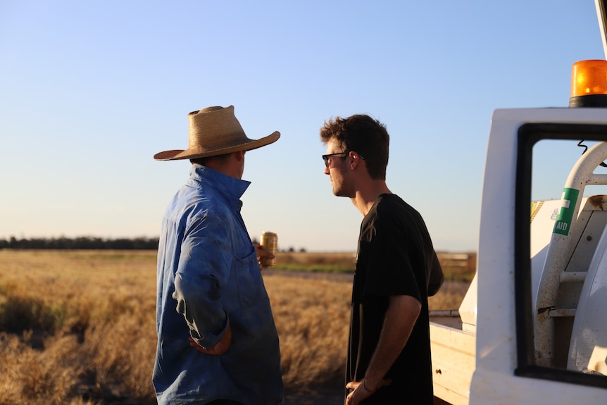 Two men stand outside a utility vehicle on a farm.