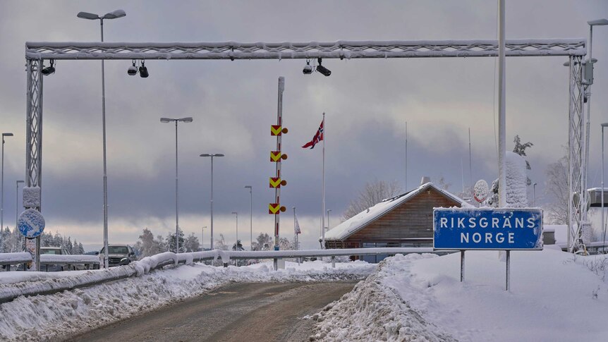 In an icy climate, a brown icy road leads to a wooden gable-roofed office with the Norwegian flag beside it.