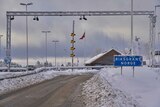 In an icy climate, a brown icy road leads to a wooden gable-roofed office with the Norwegian flag beside it.