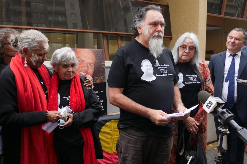 A man surrounded by family addressed a press conference outside a court with traditional Aboriginal paint on his face.