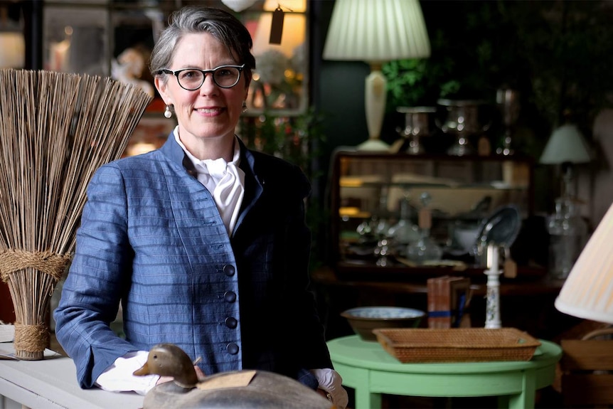 A woman stands in an antique shop and smiles at the camera