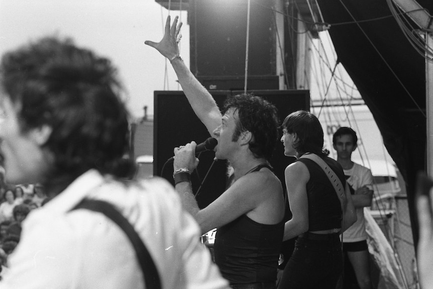 Black and white image of a man in a black vest singing to the crowd
