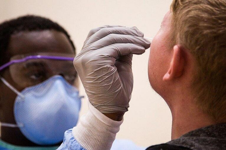 A doctor in personal protective equipment administering a SARS COVID-19 rapid antigen test on a person