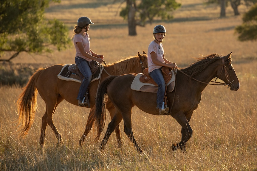 Two girls ride on two rehomed horses in a field.