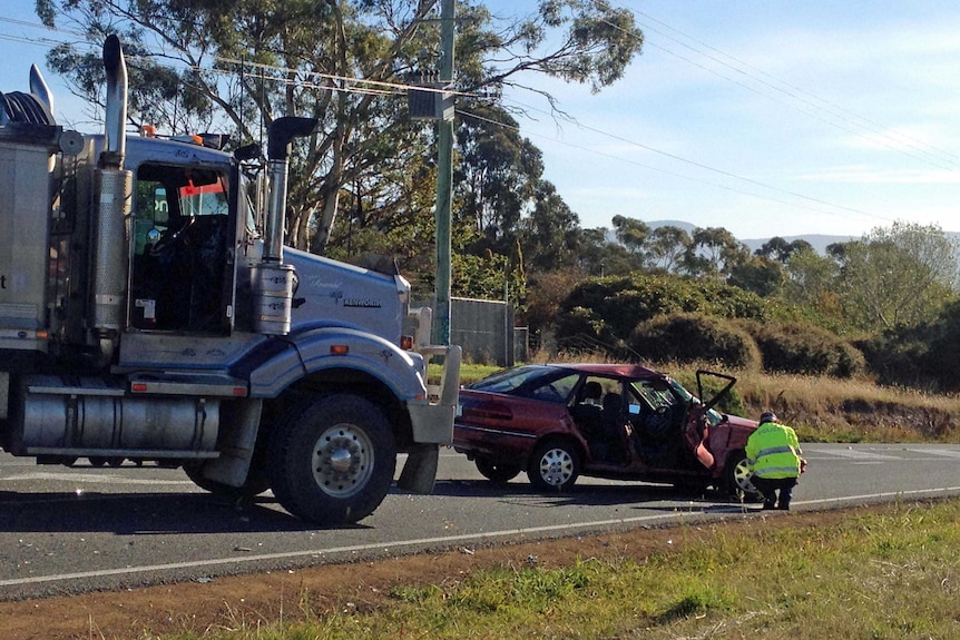 A police officer inspects a car involved in a fatal crash with a truck near Hobart.