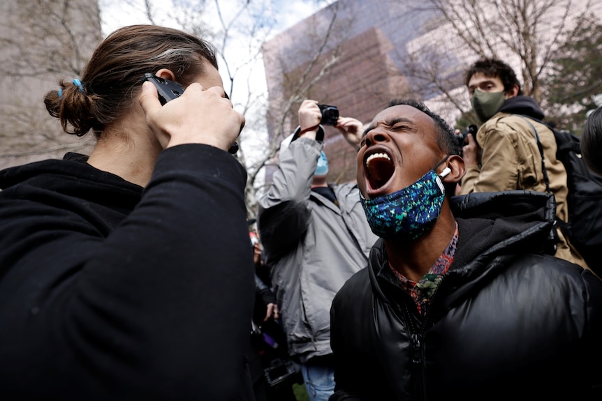 A man yells for joy while a person talks on their phone in a street demonstration