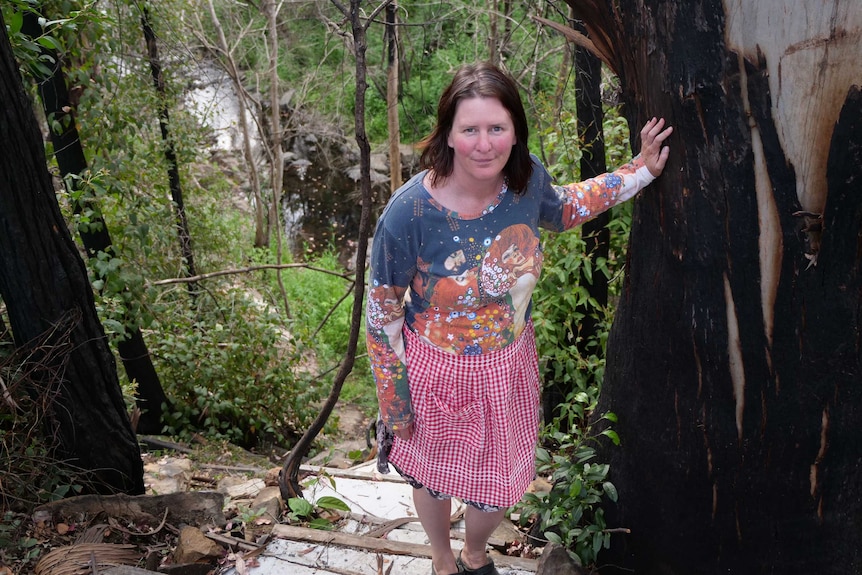 Emma standing on steep staircase to the the creek holding the large trunk of a burnt gumtree