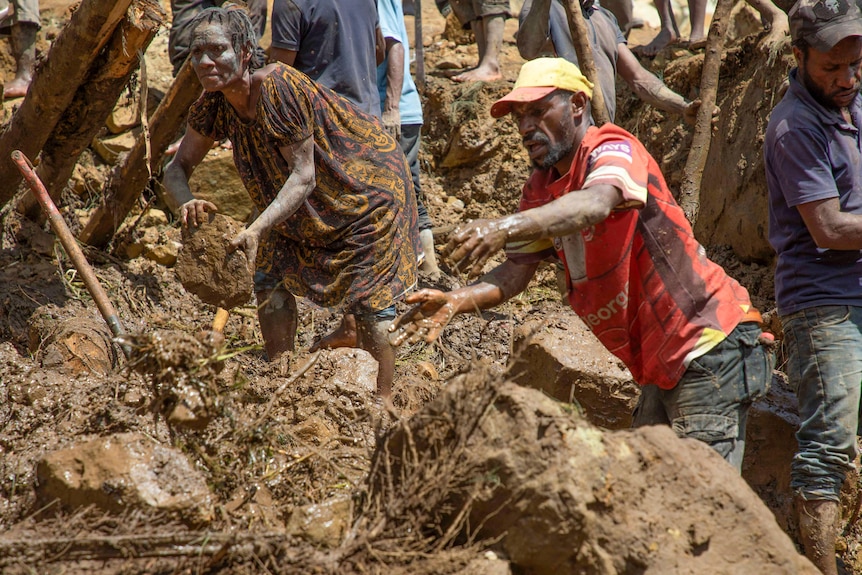 A woman and a man dig through thick, wet mud with their hands in the sun looking pained
