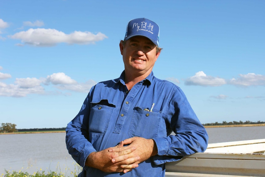 A man in a blue shirt leaning on a utility tray in a paddock.