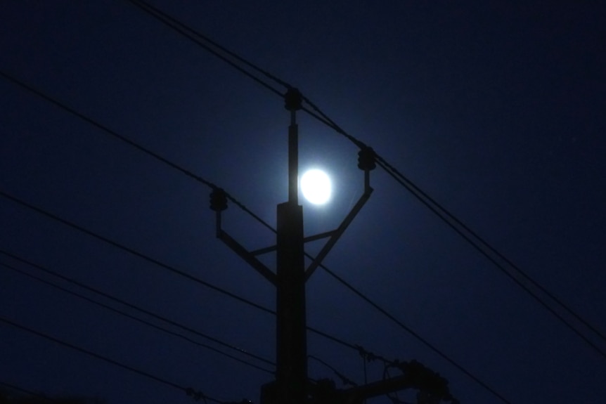 The silhouette of a power pole against the moon.