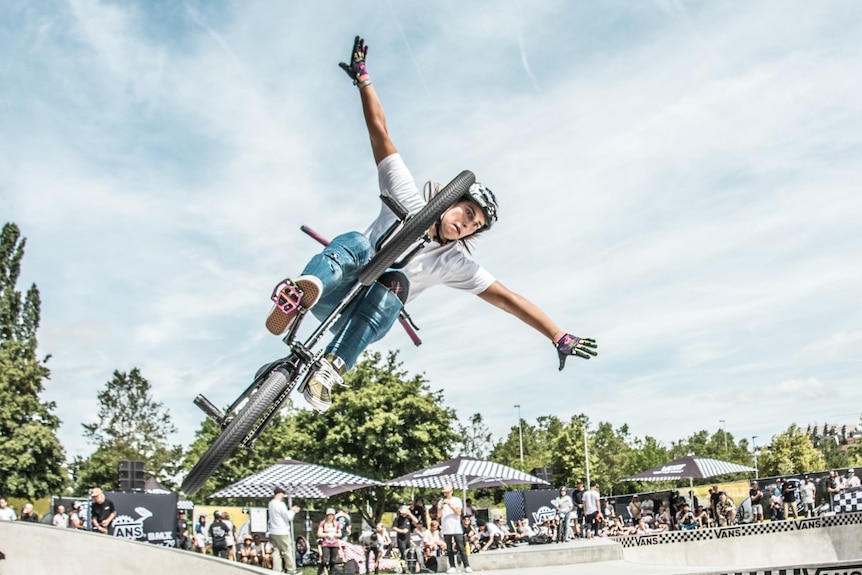 A woman spreading her arms as she pulls a trick on an airborne bicycle
