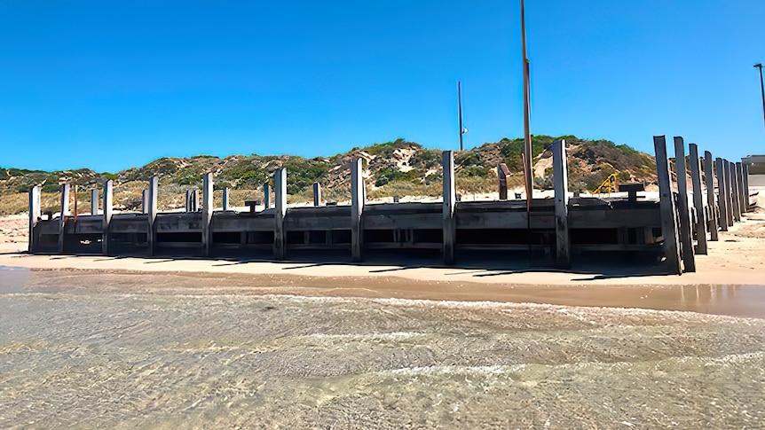 A wooden jetty stands surrounded by sand. 