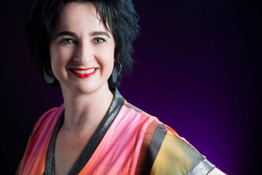 Ginger Gorman, in a bright multi-coloured top smiling at the camera and wearing bright red lipstick