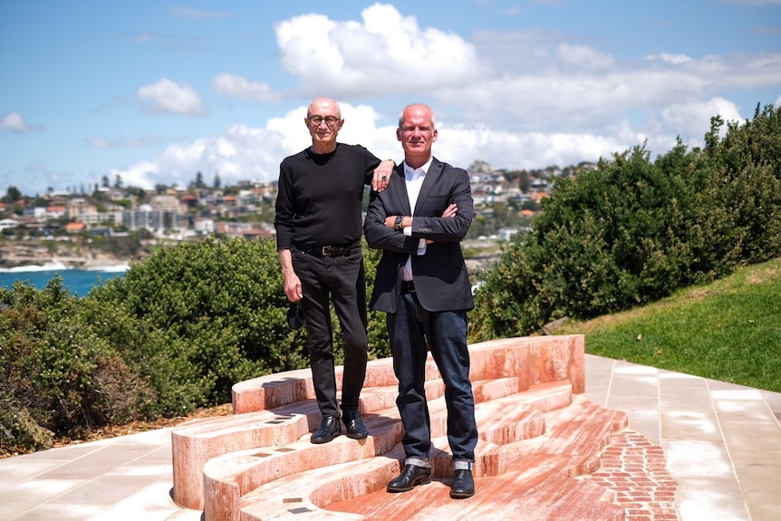 two men standing on a sandstone memorial beside the beach