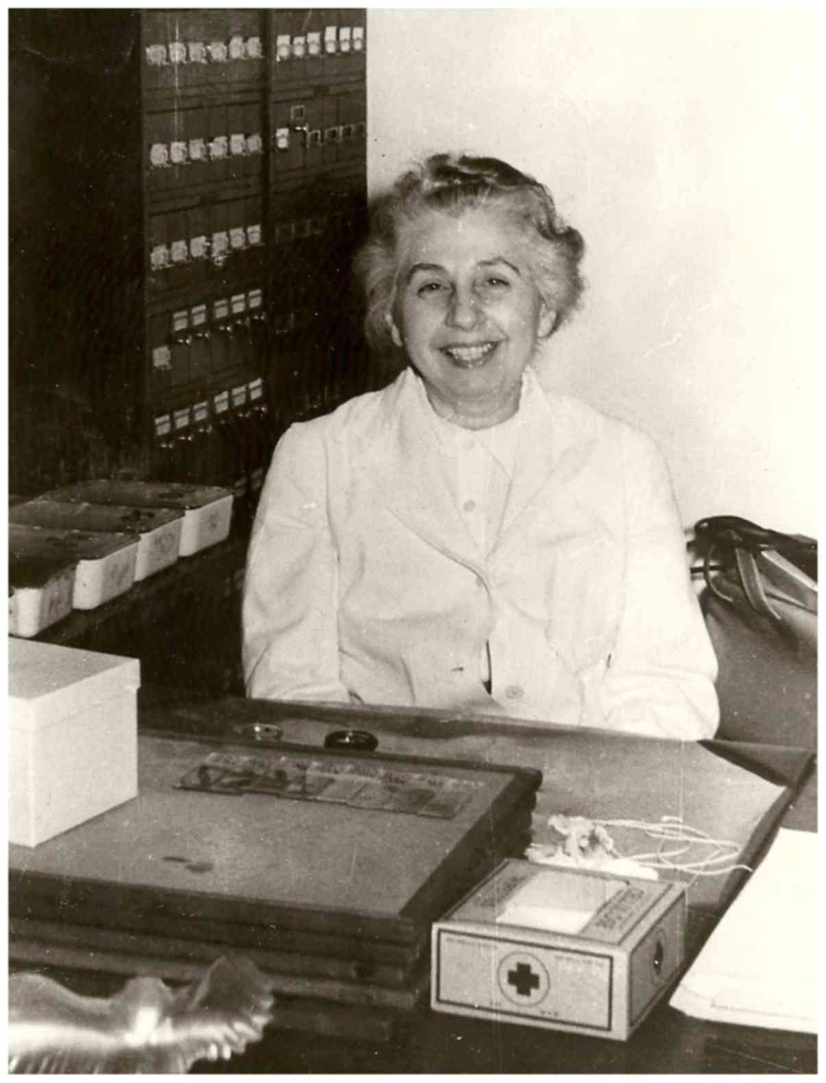 A black and white photo of a smiling woman sitting behind a desk