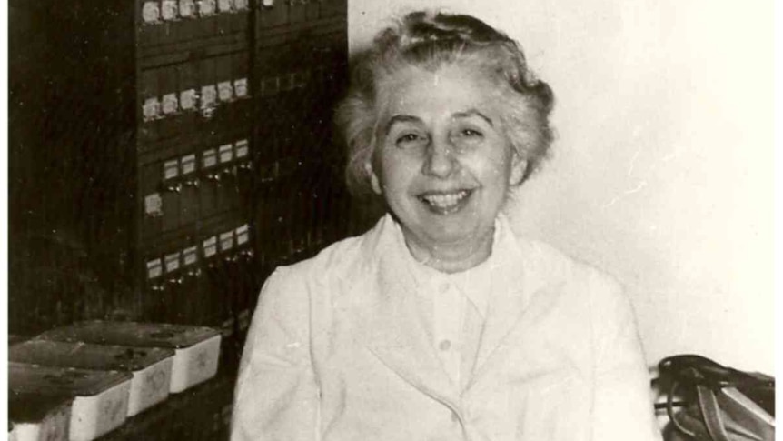 A black and white photo of a smiling woman sitting behind a desk