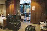 Dan looks out the window of his nursing home room with a single bed, leather armchair in foreground