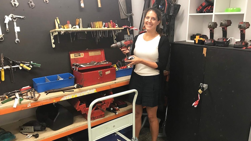 Rachel Bryson holds a drill while standing in front of other tools at the Brisbane Tool Library.