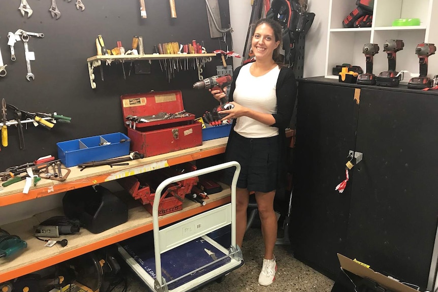 Rachel Bryson holds a drill while standing in front of other tools at the Brisbane Tool Library.