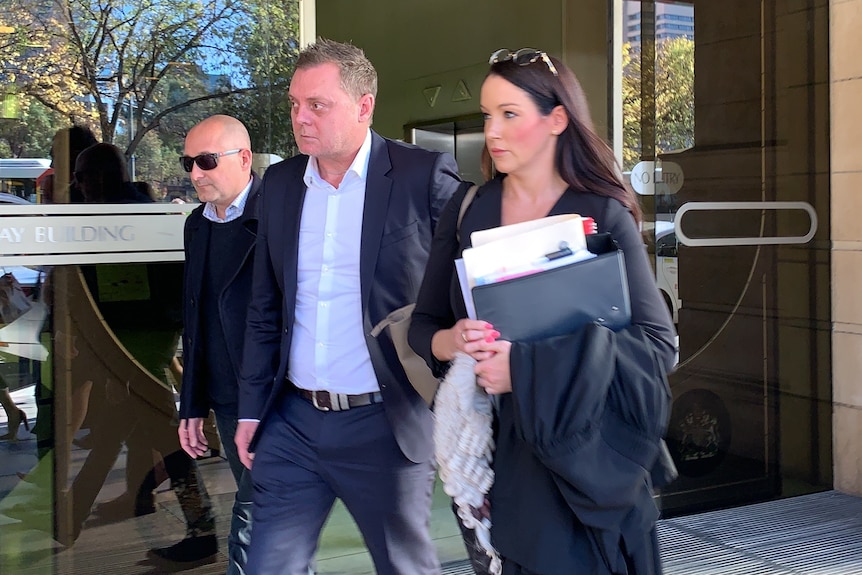 A man leaves a court building with two women beside him