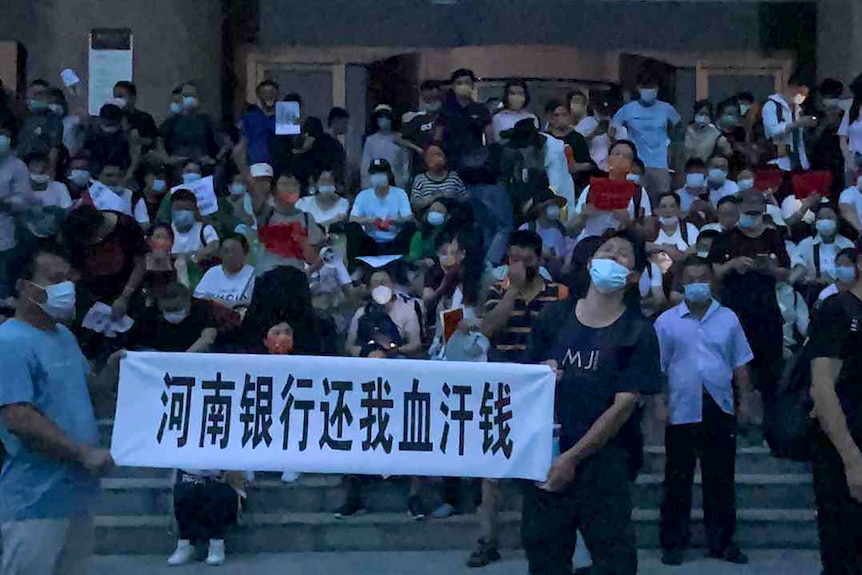 People wearing face masks stand on steps holding banners