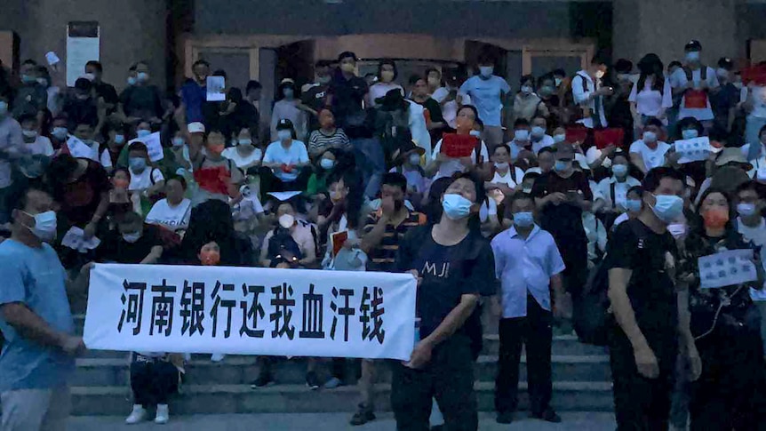 People wearing face masks stand on steps holding banners