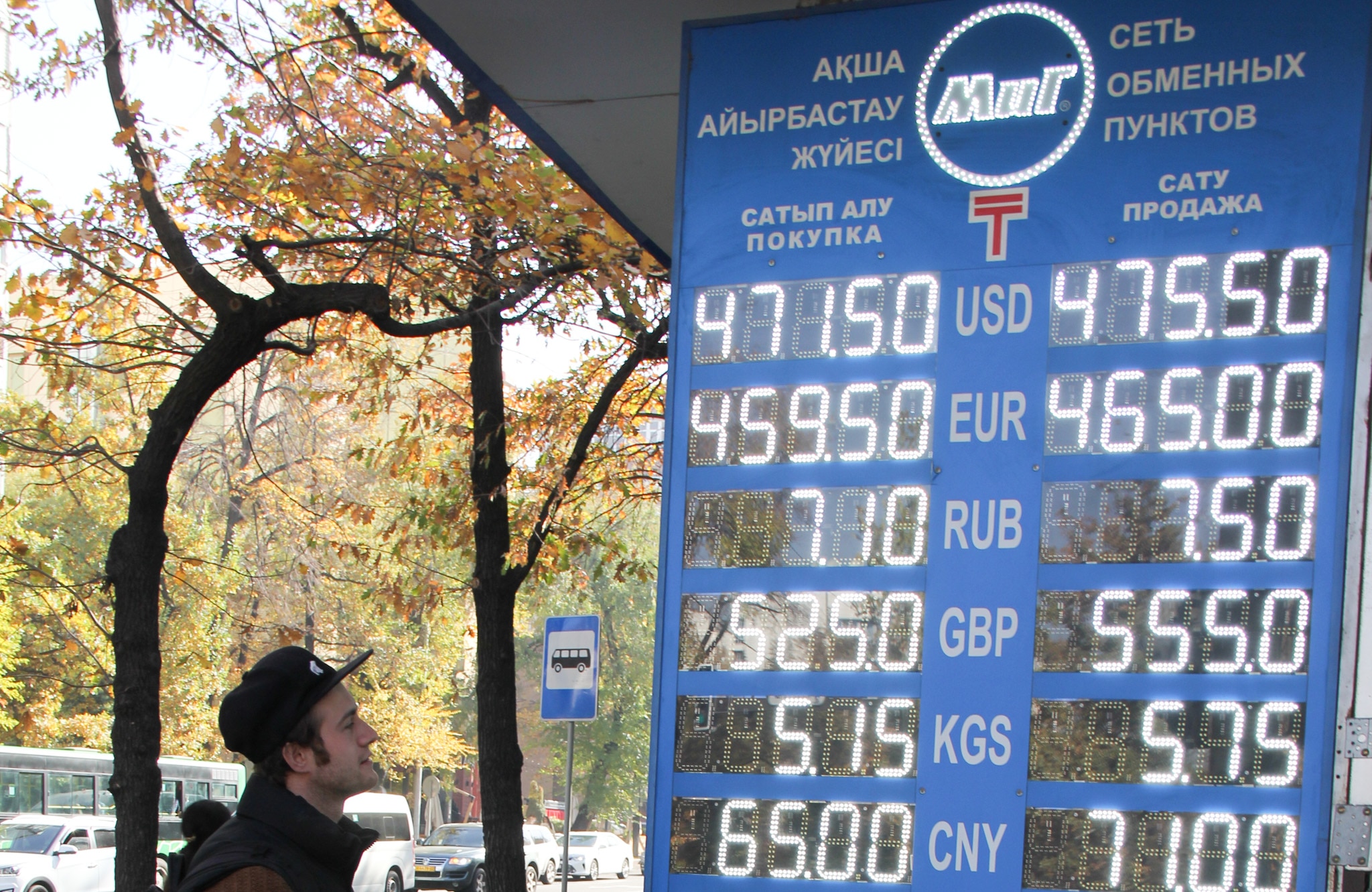 A sign displaying different exchange rates in US, Euro and Russian with trees in the background.