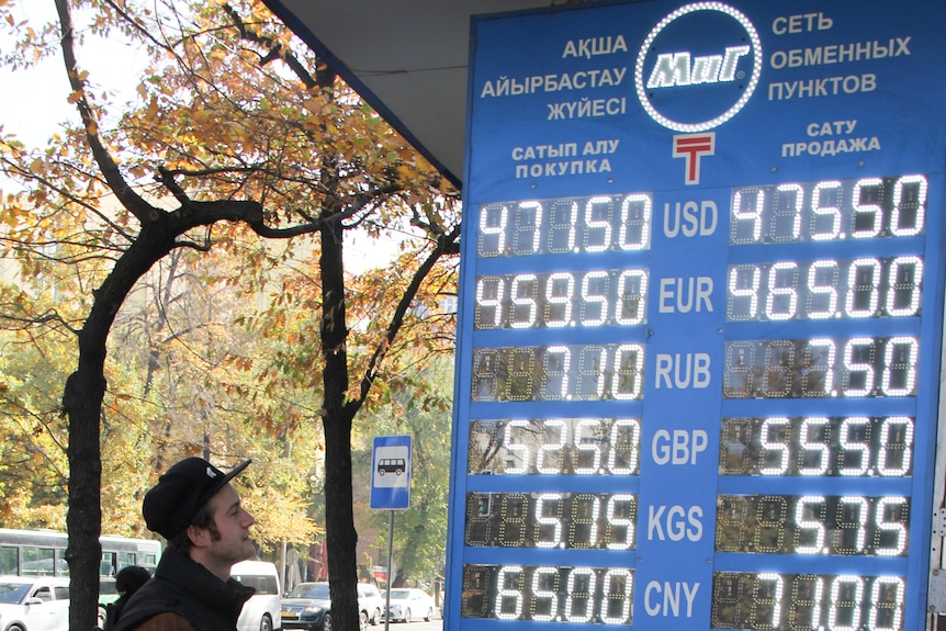 A sign displaying different exchange rates in US, Euro and Russian with trees in the background.