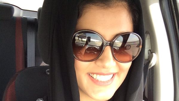 A self-portrait of Loujain Houthlou, who is smiling while driving and wearing sunglasses and a head scarf.