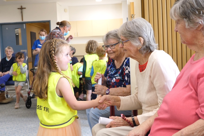 A young girl shakes an older woman's hand, in a retirement village.