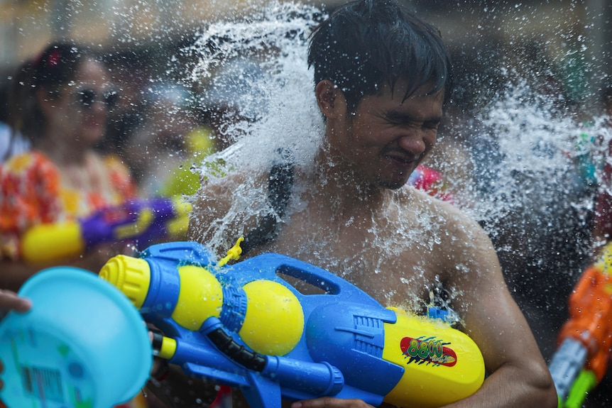 A topless reveller armed with a neon waterpistol closes his eyes as he is hit with a big spray of water.