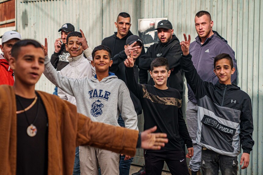 A group of teenaged boys stand together, some showing peace signs to camera, many smiling
