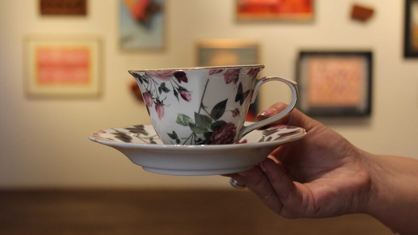 A hand holding a tea cup inside an art exhibition
