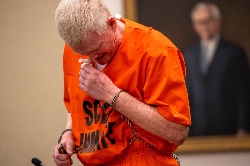 A man in handcuffs and a prison jumpsuit wipes tears from his eyes 