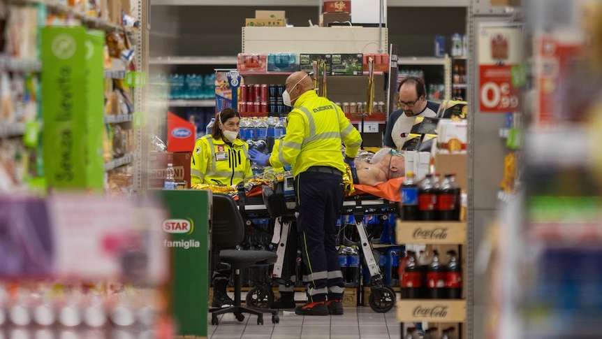 Medics stand beside an injured person on a stretcher in a supermarket.