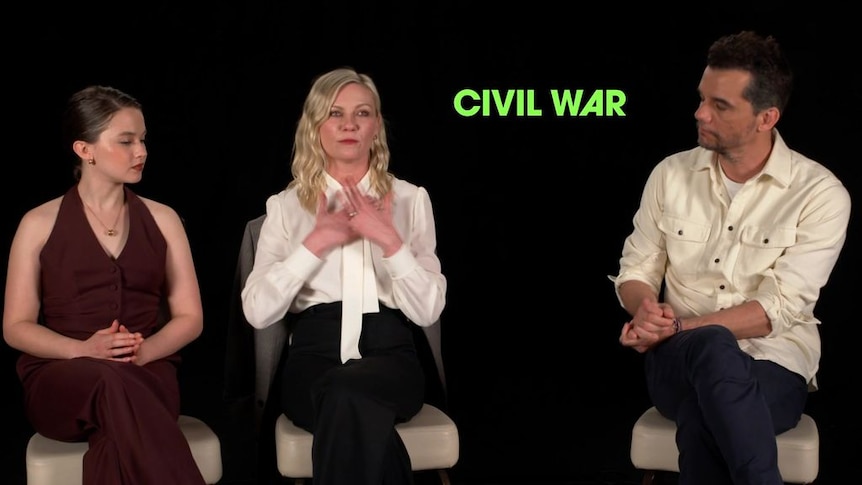 Actors on a press junket give an interview with 'Civil War' branding behind them.