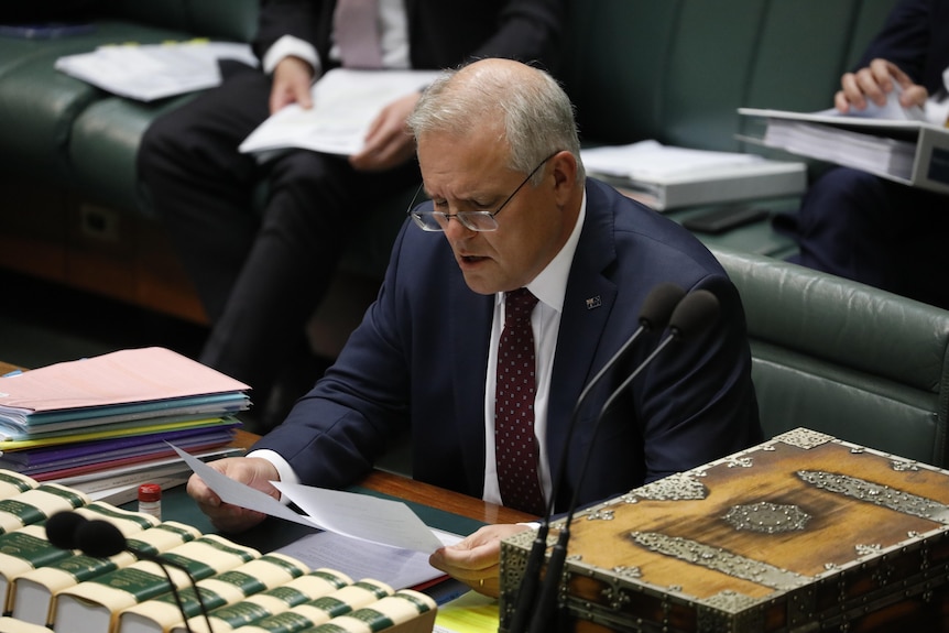 Scott Morrison reads from two pieces of paper while sitting in the House of Representatives 