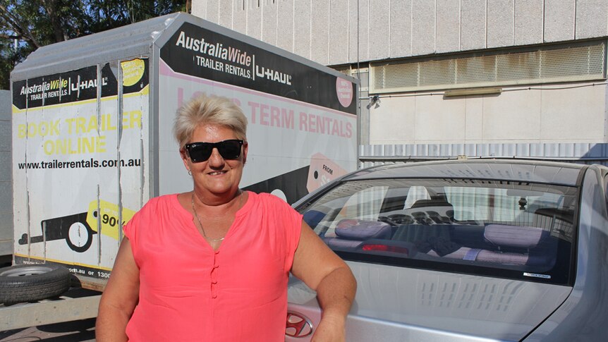 A woman stands in front of silver car at a petrol station in Darwin.