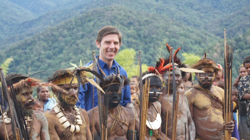 Eric Tlozek stands among villagers in tribal dress in front of mountains