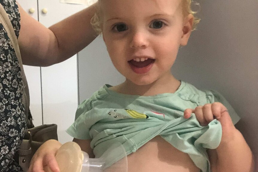 Toddler lifting up shirt with breast pump in hand.